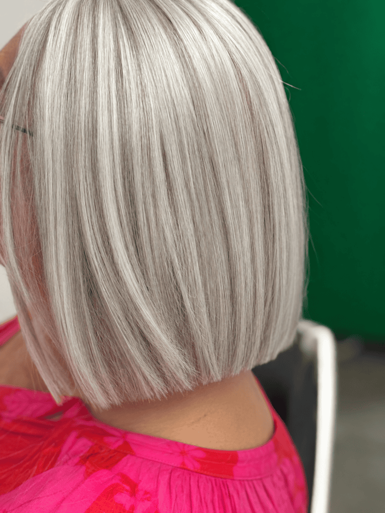 Nahaufnahme der Seiten- und Rückansicht eines kinnlangen, stumpf geschnittenen silbergrauen Bobs mit glänzender Oberfläche vor grünem Hintergrund.