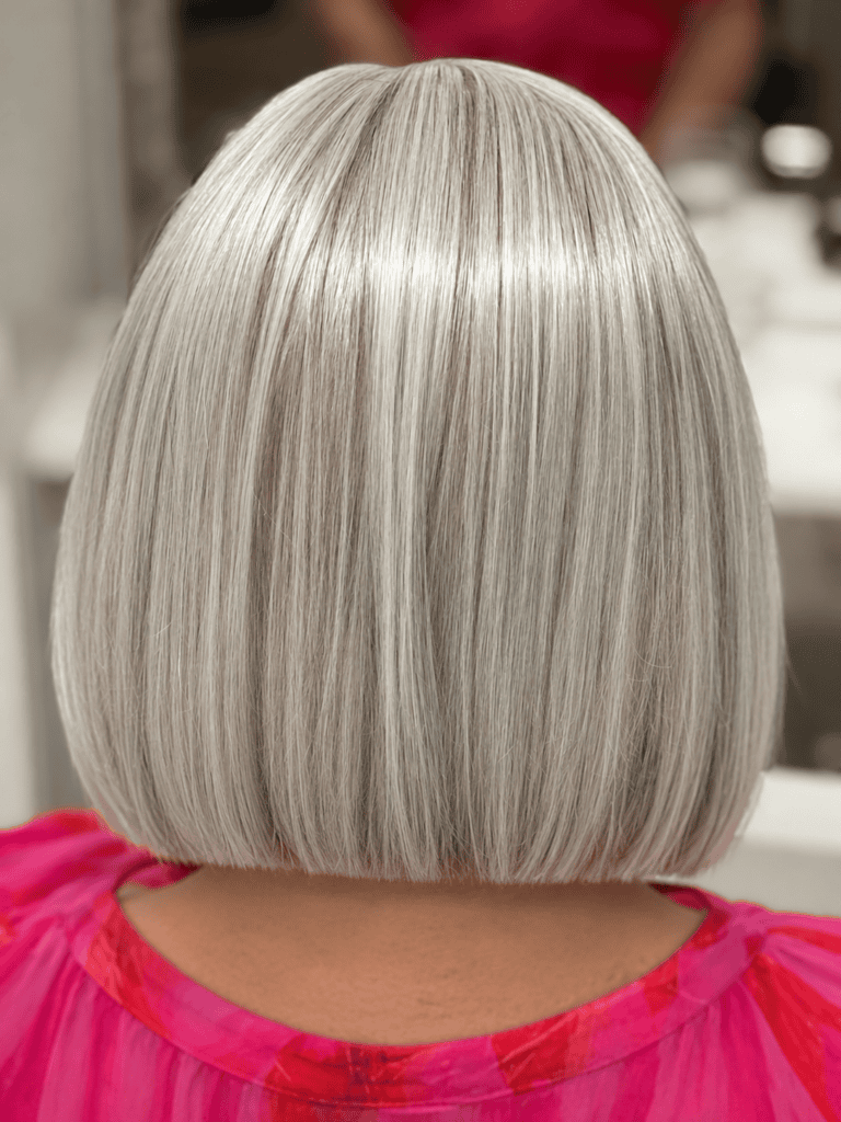 Eine Nahaufnahme der Rückansicht eines präzisen, silbergrauen Bob-Haarschnitts mit geradem Saum. Die Person trägt ein rosa gemustertes Oberteil vor einem unscharfen Salon-Hintergrund.